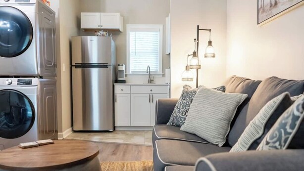 A compact living space with a kitchenette, a washing machine, a refrigerator, and a sofa with patterned cushions. - Skip the hotel. Stay 4 min from Maxwell, walk to downtown & Civil Rights landmarks, and bring your dog. (Montgomery)