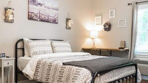 A bedroom with a bed, bedside table, lamp, and a painting on the wall. - Skip the hotel. Stay 4 min from Maxwell, walk to downtown & Civil Rights landmarks, and bring your dog. (Montgomery)