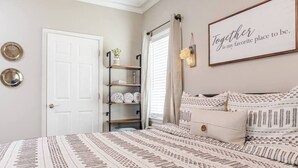 Une chambre à coucher avec un lit, une étagère avec des serviettes, une porte et un mur sur lequel est accroché un panneau.