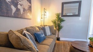Un salon comprenant un canapé, une table basse, une plante en pot, une carte du monde accrochée au mur et un miroir.