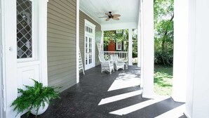 A covered porch with white railings and a ceiling fan, leading to a house with a dark porch floor and a green plant by the door. - Made for the trips that bring everyone together. This historic Montgomery home gives families, wedding parties, and groups room to gather, room to disappear for a while, and one place to come back to—all minutes from downtown, Maxwell AFB, and the re (Montgomery)