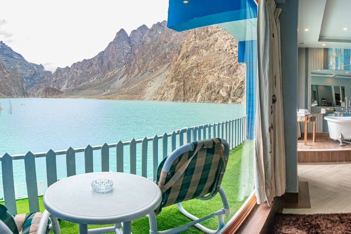Habitación con vistas a un lago y montañas, bañera, zona de comedor con mesa y sillas, y sala de estar con sofá y cojines.