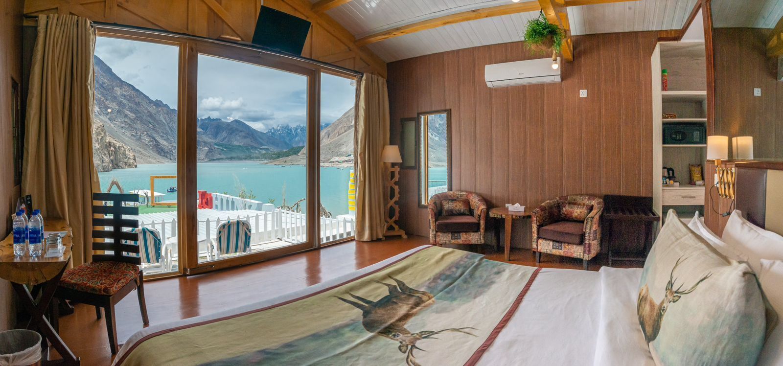 A room with a large bed, a view of a lake, and a balcony with chairs.