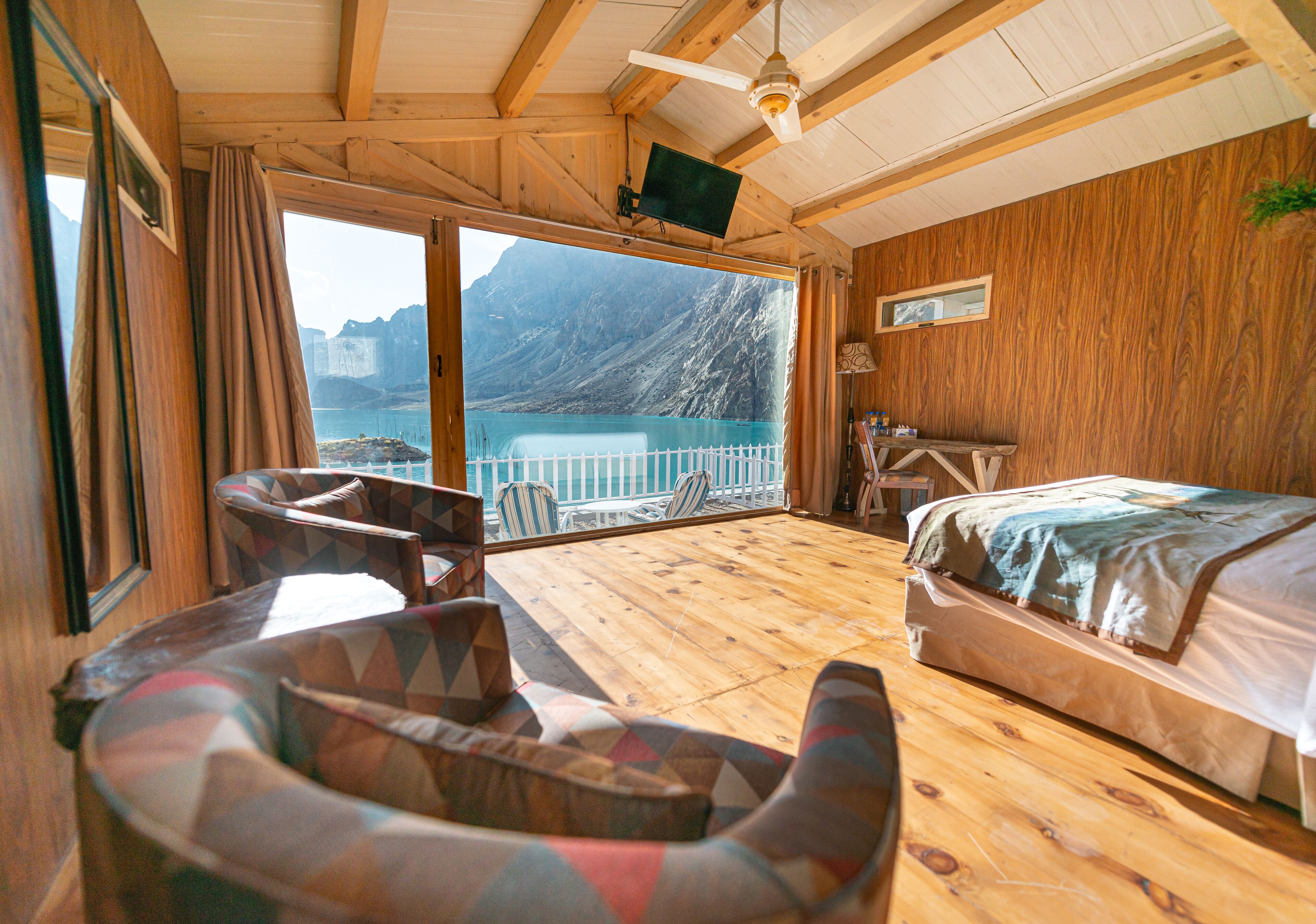 A wooden cabin with a balcony, a bed, a sofa, and a TV.