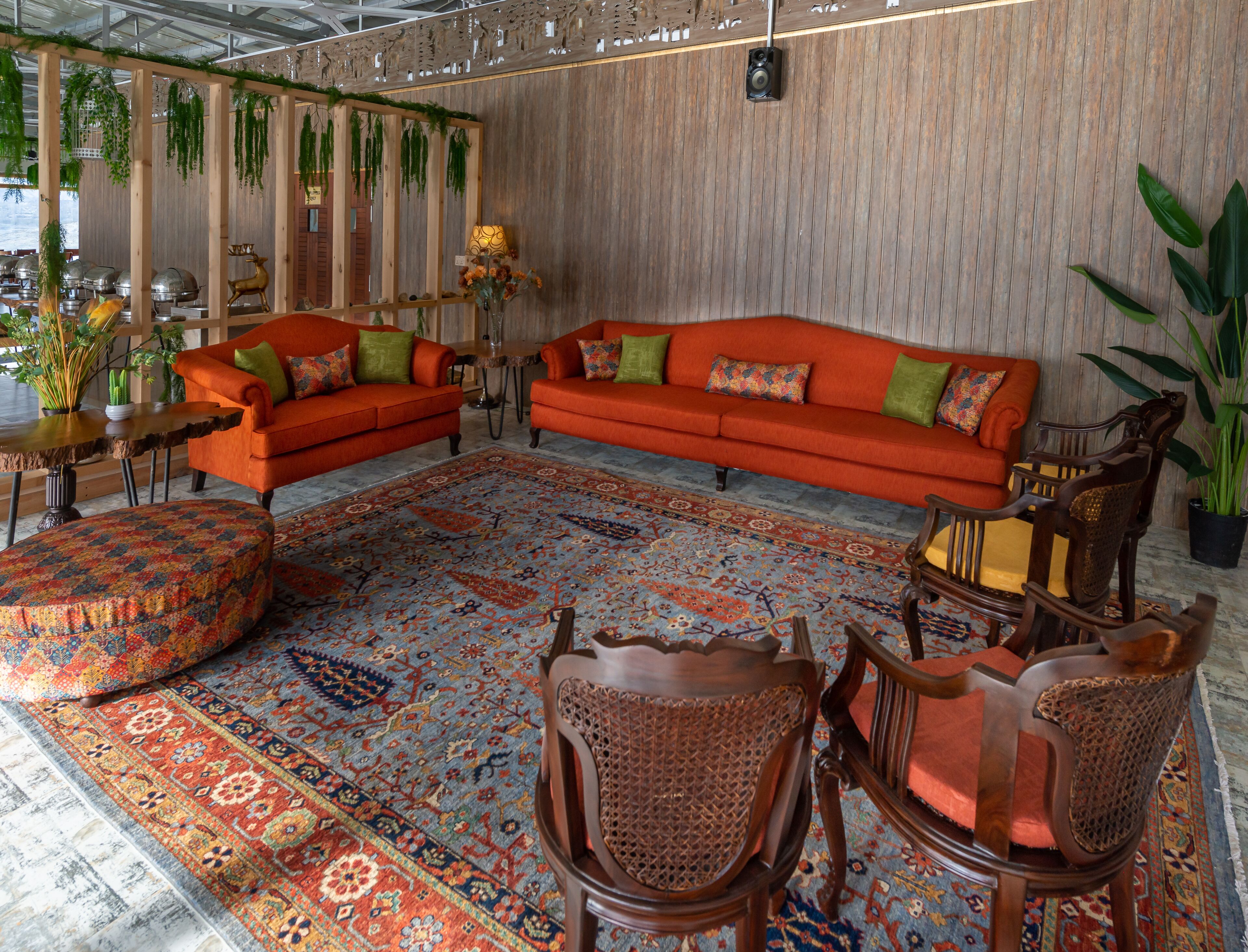 A cozy living room with a large orange sofa, two armchairs, a wooden coffee table, and a patterned rug.