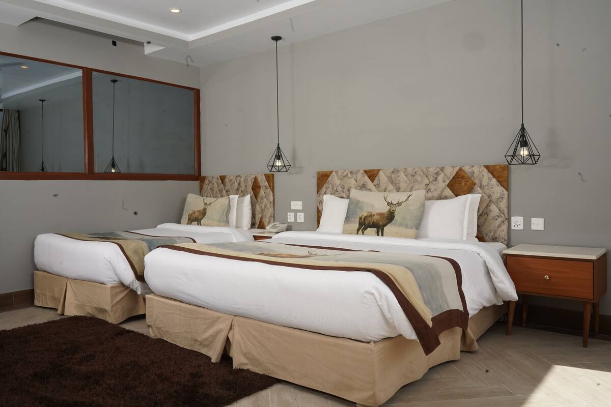 Cama doble con cabecera estampada con ciervo, mesita de noche y un espejo grande en la pared.