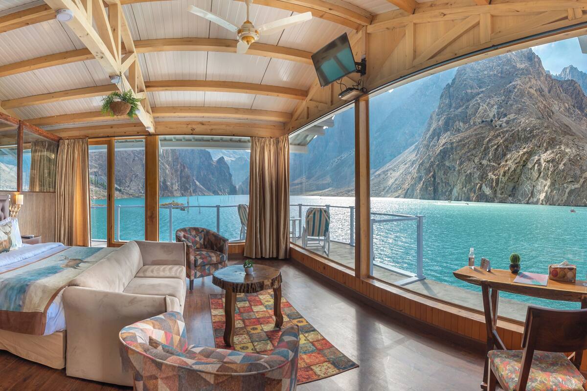 Amplia habitación con una cama grande, un sofá, una mesita y una silla. Una ventana grande ofrece vistas al mar y a las montañas.