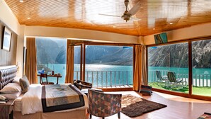 Een slaapkamer met een groot bed, een bureau en een stoel, met uitzicht op een schilderachtig meer en bergen.