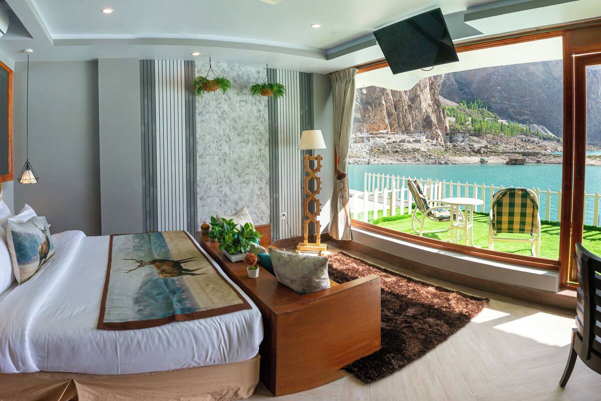 Un dormitorio moderno con una cama grande, un escritorio y vistas a un lago y montañas.