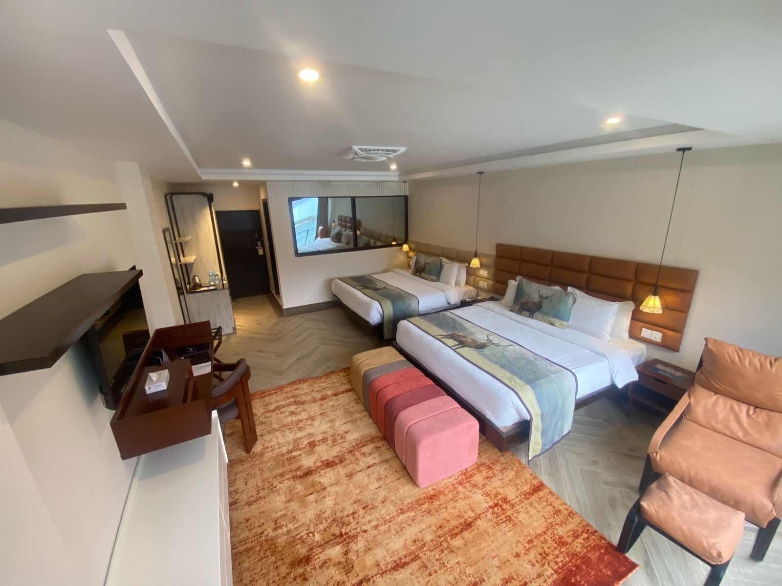 A hotel room with two beds, a desk, a chair, a small table, and a mirror.