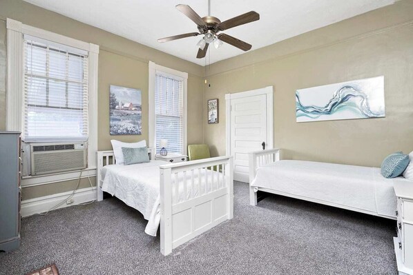 A bedroom with two single beds, a ceiling fan, and artwork on the walls.