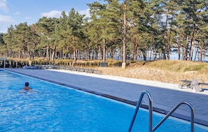 Une piscine où une personne nage, entourée d’arbres et bordée d’une allée pavée.