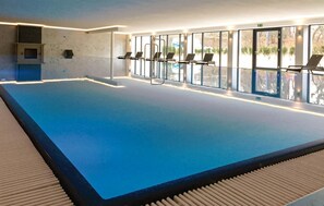 Ein Hallenbad mit großen Glaswänden, Liegestühlen und Blick ins Freie.