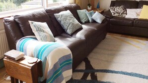 A living room with a brown leather sofa, a wooden side table, and a patterned rug. - Detached House, 2 Bed, Sleeps 4, Parking (Fowey)