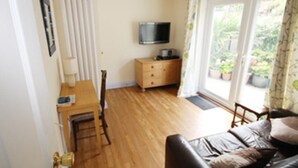A cozy living room with a wooden floor, a sofa, a TV on a wooden cabinet, and a door leading to a balcony with potted plants. - Detached House, 2 Bed, Sleeps 4, Parking (Fowey)