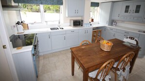 A kitchen with white cabinets, a wooden table, and a microwave. - Detached House, 2 Bed, Sleeps 4, Parking (Fowey)