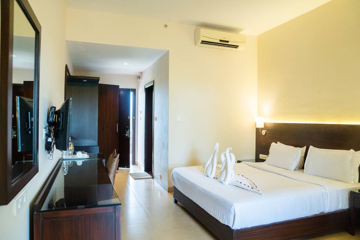 A hotel room with a bed, bedside table, mirror, and an air conditioning unit.