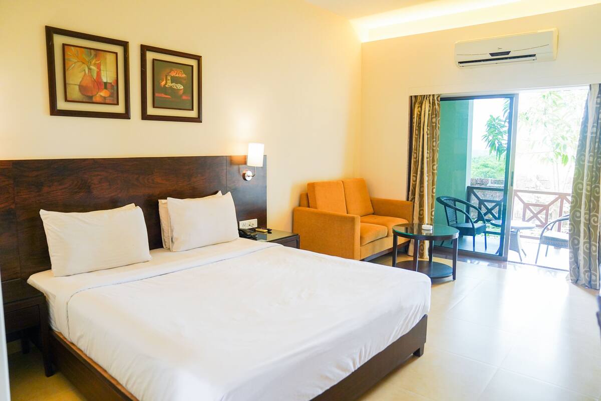 A hotel room with a large bed, a sofa, a small table, and a balcony with chairs.