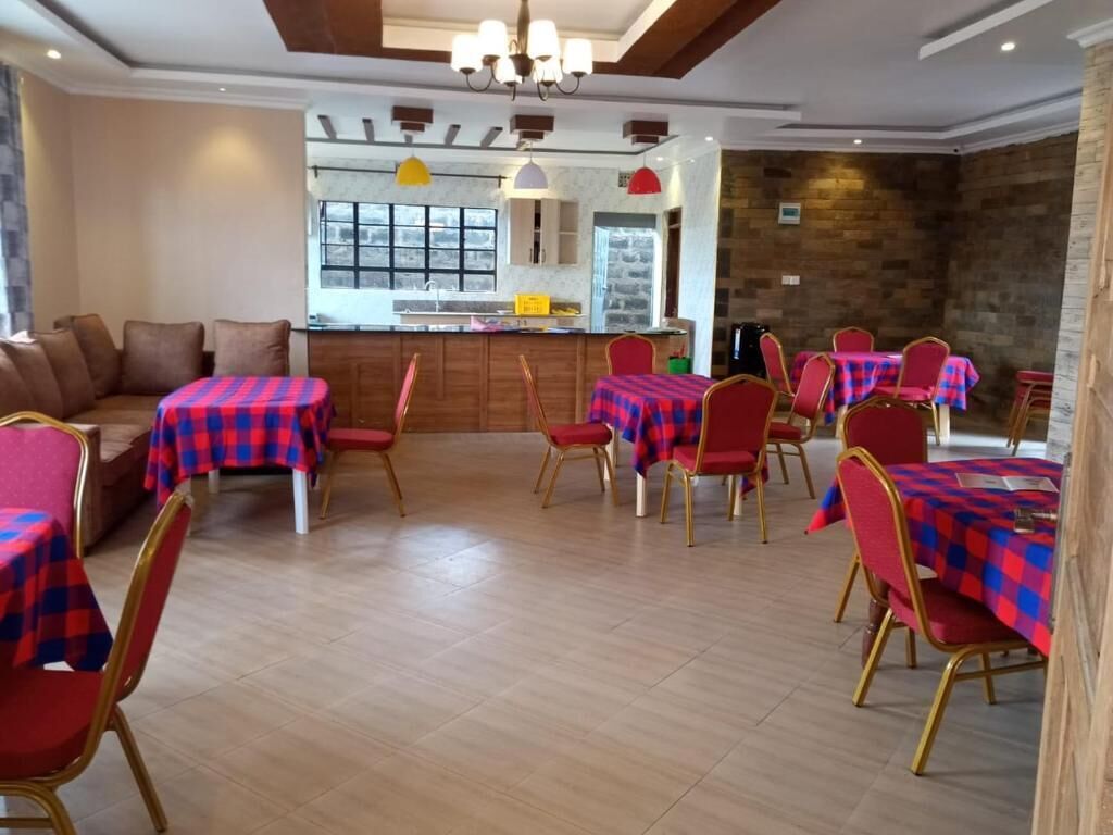 A dining area with tables and chairs, a kitchen in the background, and a stone wall.