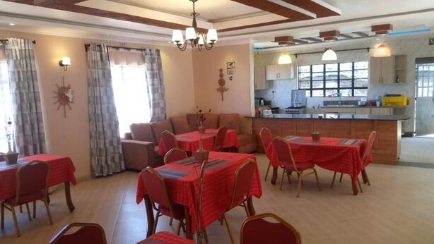 A dining area with tables and chairs, a kitchen in the background, and a chandelier. - Stay.Plus Villa Serene Hotel Kitale (Kitale)