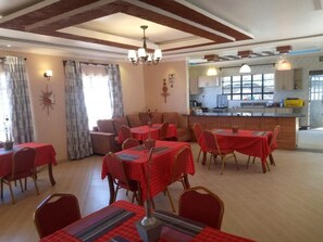 A dining area with tables and chairs, a kitchen in the background, and a chandelier. - Stay.Plus Villa Serene Hotel Kitale (Kitale)