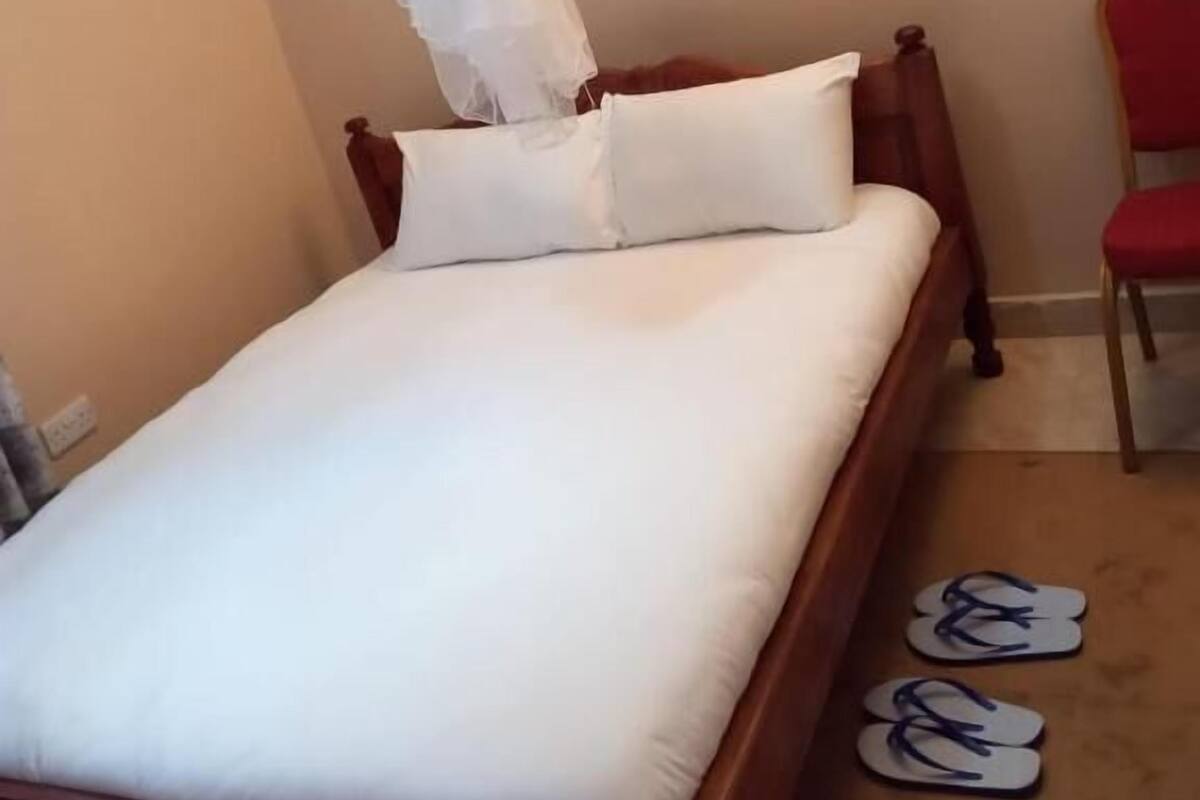 Una cama bien hecha con ropa blanca y dosel, un cabecero de madera y un par de chanclas en el suelo.