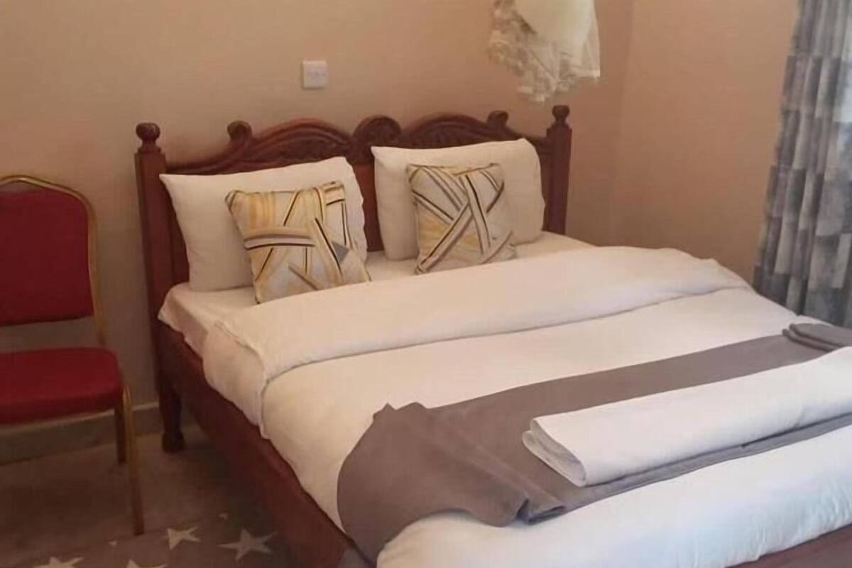Una cama bien hecha con cabecera de madera, una silla roja y un suelo con estampado de estrellas.
