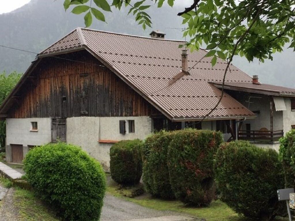 A rustic wooden barn with a sloped roof, surrounded by well-maintained hedges and a gravel path.