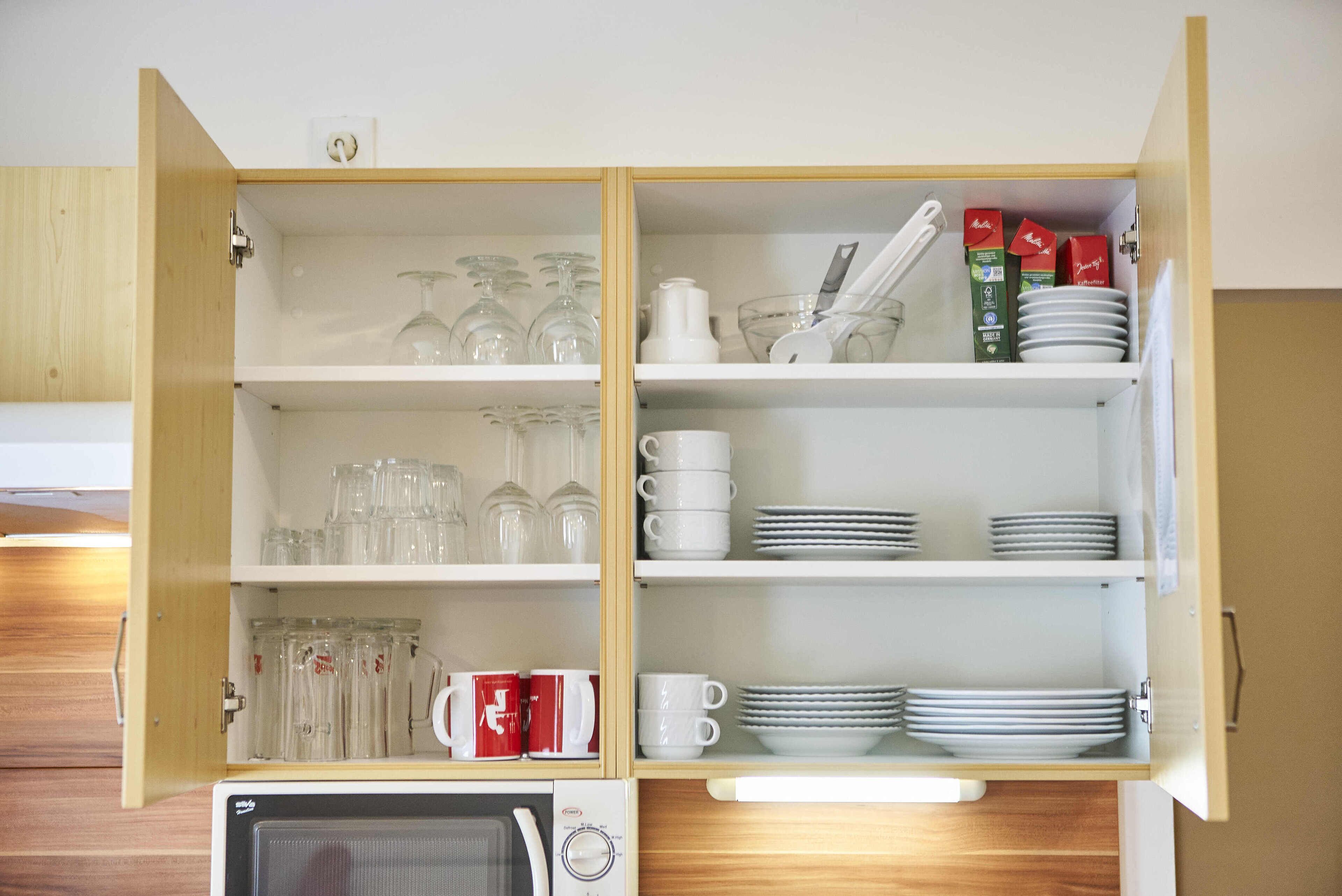 A kitchen cabinet with shelves containing glassware, cups, and plates.