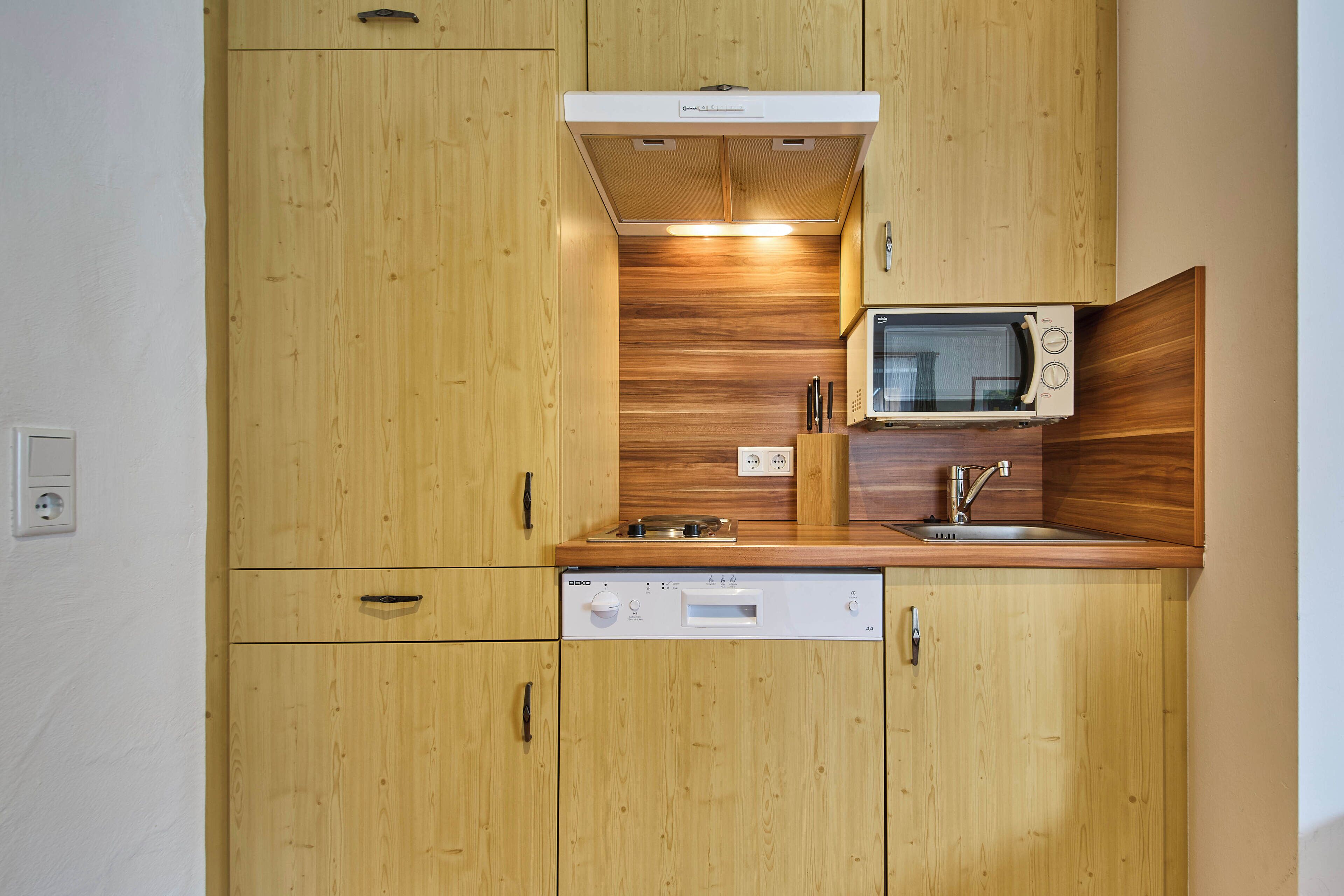 A compact kitchen with wooden cabinets, a built-in microwave, and a dishwasher.