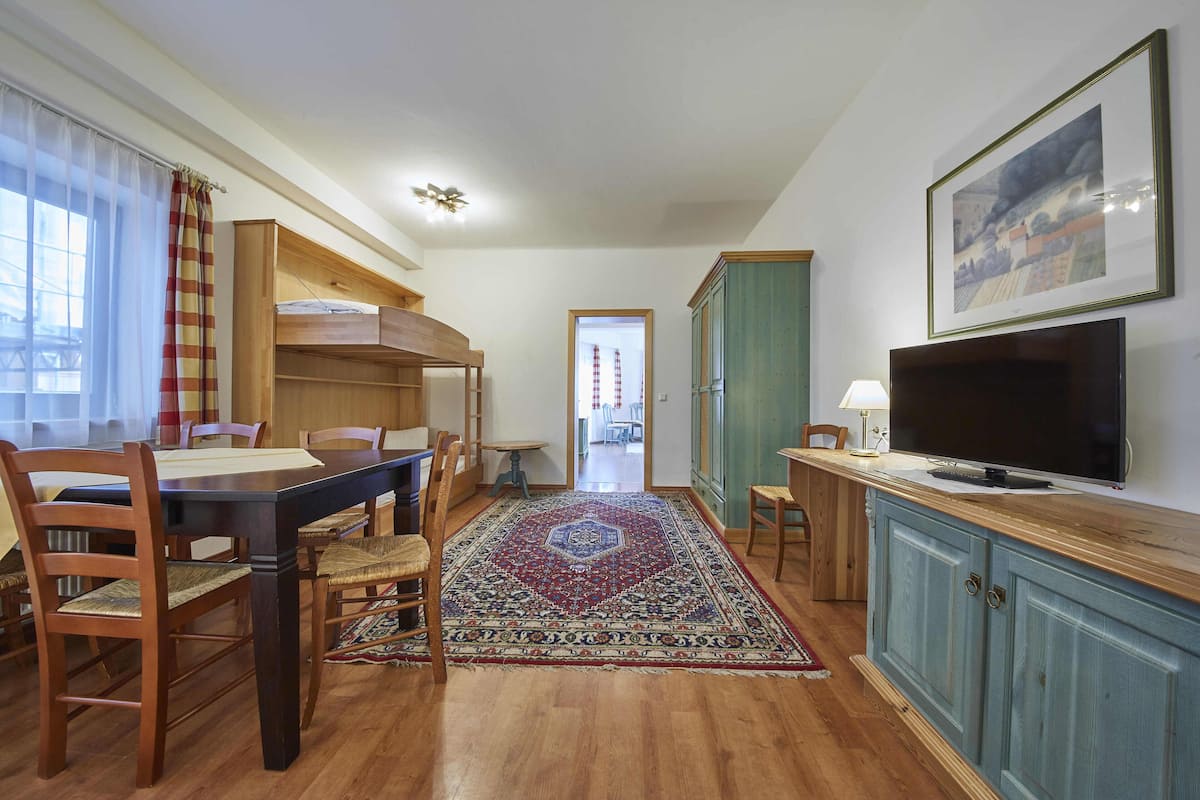 Une pièce chaleureuse avec une table à manger en bois, des chaises, un lit superposé, un téléviseur et un grand tapis.