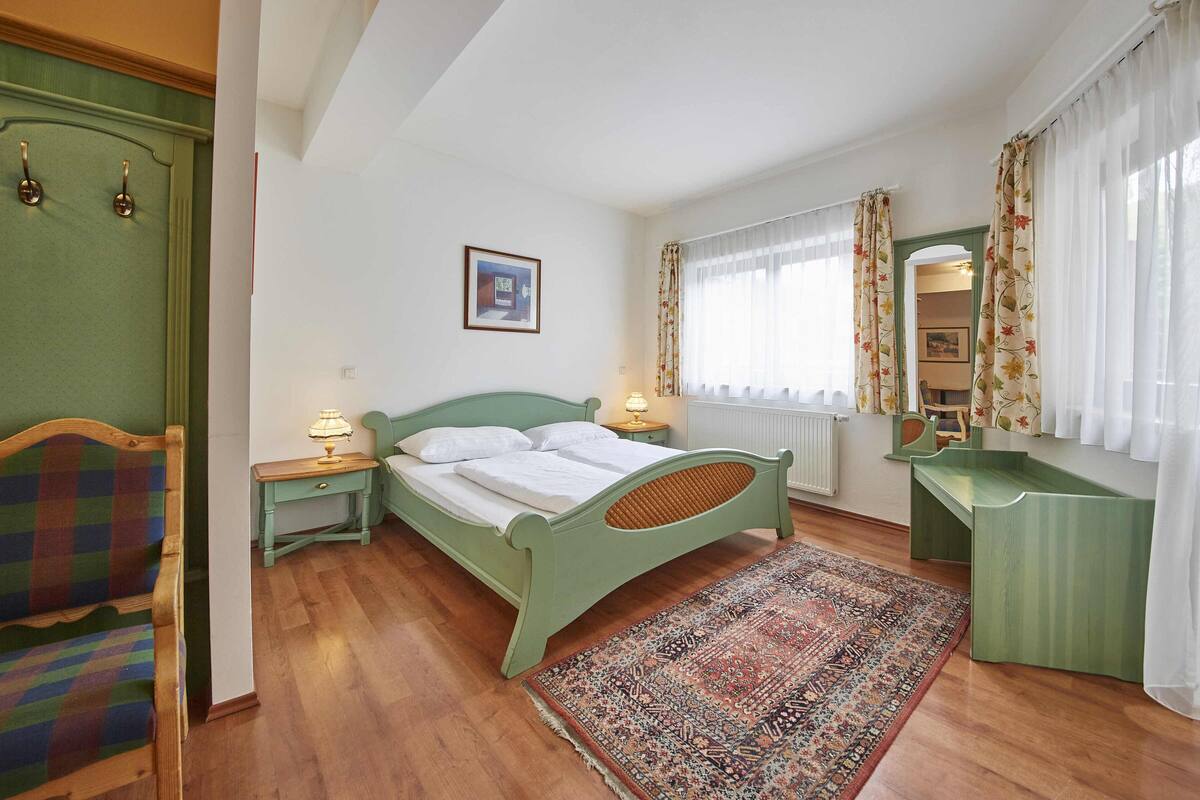 Une chambre à coucher avec un lit, des tables de chevet, un miroir, une fenêtre avec des rideaux et un tapis à motifs.