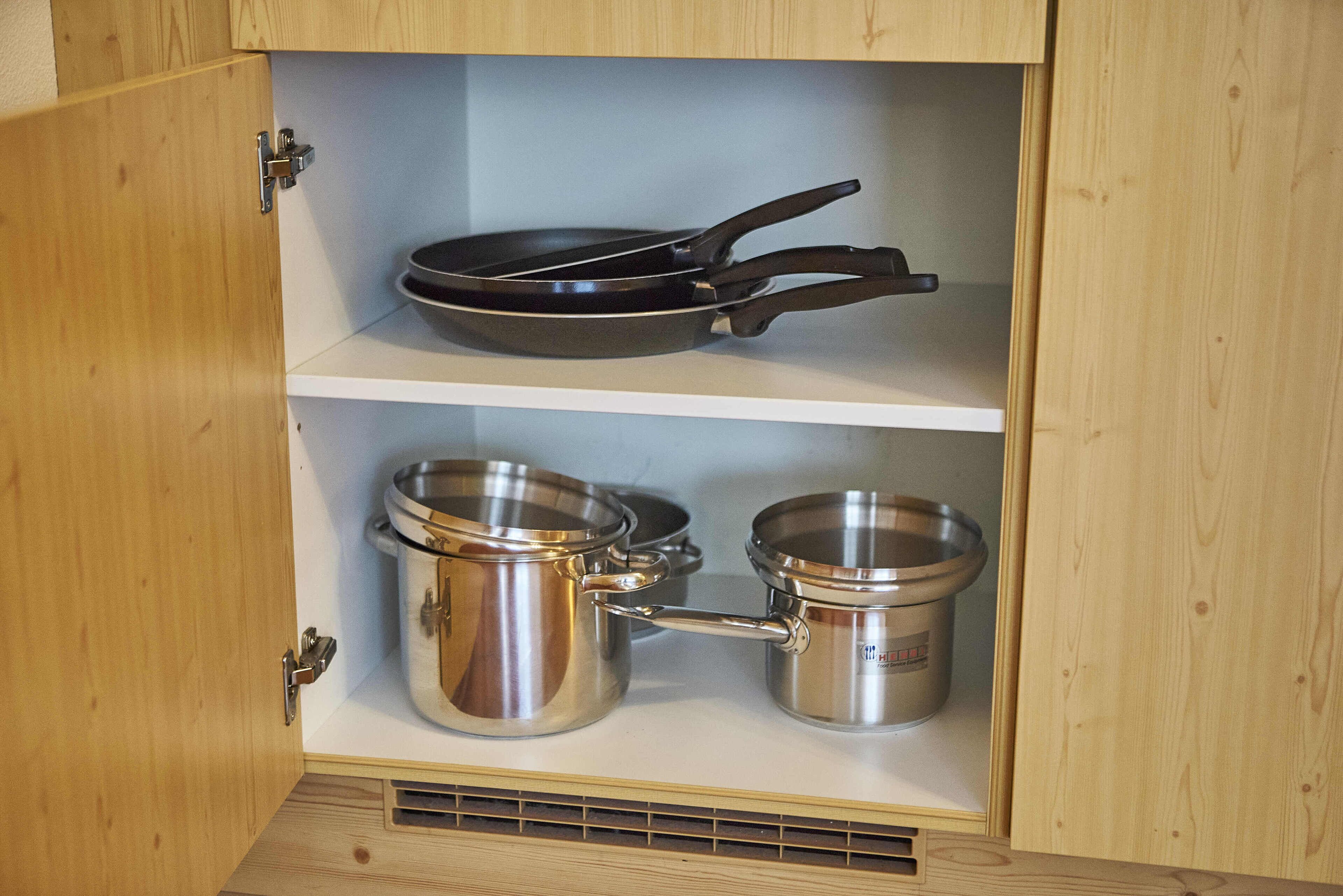 Un meuble de cuisine avec une poêle sur l’étagère supérieure et des casseroles en acier inoxydable sur l’étagère inférieure.