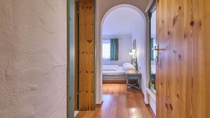 Un pasillo que conduce a un dormitorio con puerta de madera, cama y mesita de noche con lámparas.