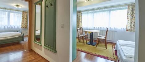 A hotel room with a bed, a dining table with chairs, a mirror, and a window with curtains.
