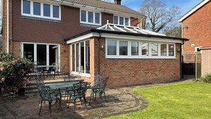 A brick house with a conservatory, a patio with a table and chairs, and a well-maintained lawn. - Sherpa (Romsey)