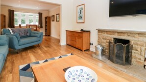 A living room with a sofa, a coffee table, a fireplace, and a television mounted on the wall. - Sherpa (Romsey)