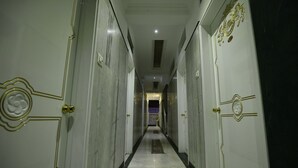 Un long couloir étroit aux murs et aux portes en marbre, qui mène à une pièce au fond.