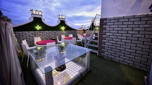 Une table avec un plateau en verre, des chaises, un mur en briques et un escalier.