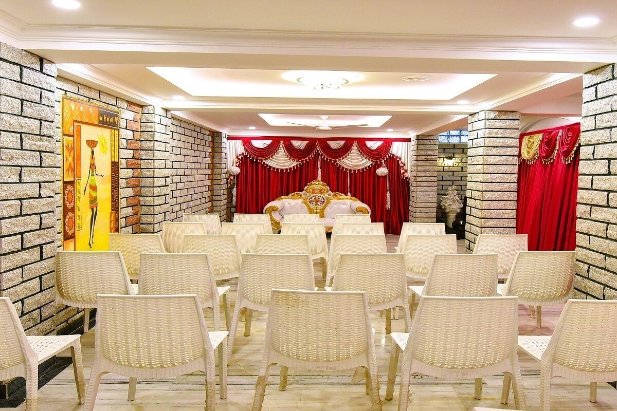 A room with a large bed, white chairs arranged in rows, and red curtains.