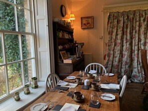 A dining room with a wooden table set for four, surrounded by white chairs. A bookshelf with various items is visible in the background. - Red Lodge Country House (King's Lynn)