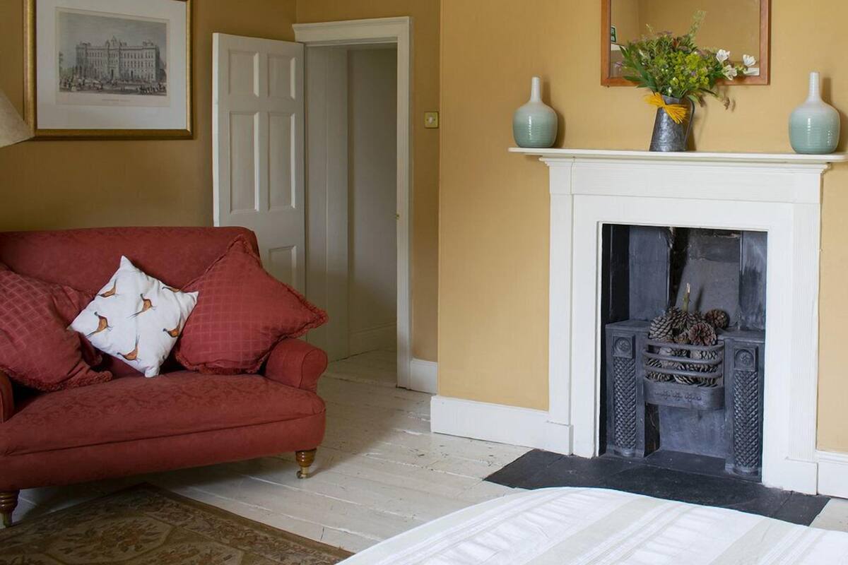 A room with a red sofa, a white bed, a fireplace, and a framed picture on the wall.
