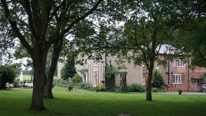 Une zone herbeuse avec des arbres et, au fond, un bâtiment en briques.