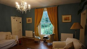 Une pièce avec un lustre, une fenêtre ornée de rideaux jaunes, une porte blanche et un radiateur.