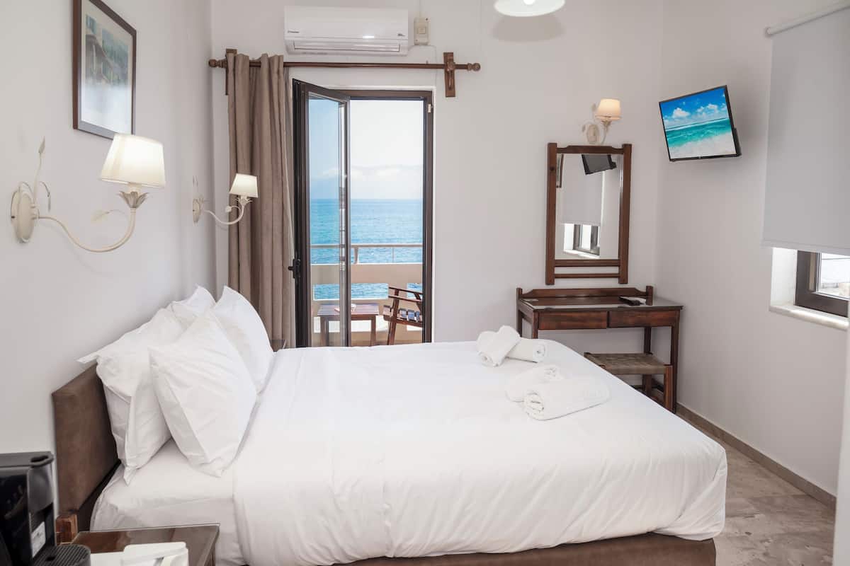 Habitación de hotel con cama, escritorio con silla, ventana con vista al mar y televisor de pared.