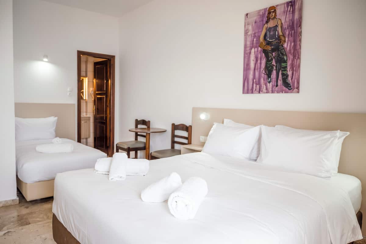 Habitación de hotel con dos camas, un cuadro en la pared, una puerta de madera y una pequeña mesa.