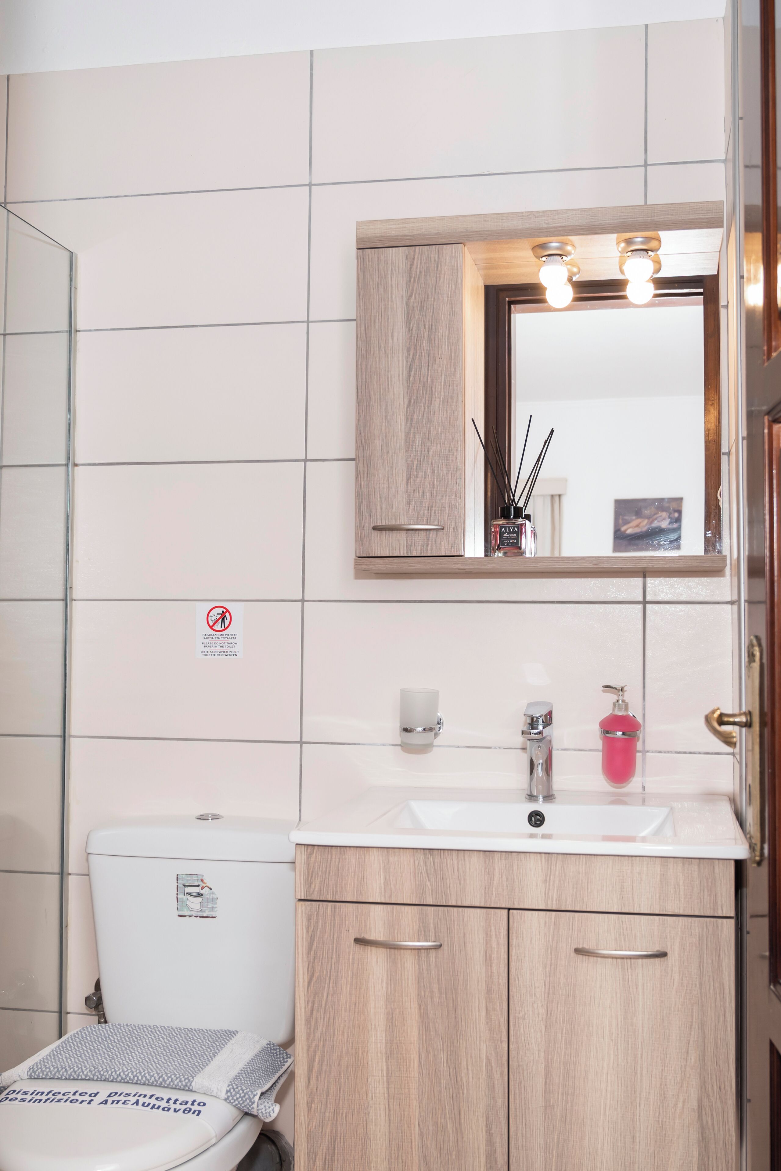 A bathroom with a toilet, sink, mirror, and cabinets.