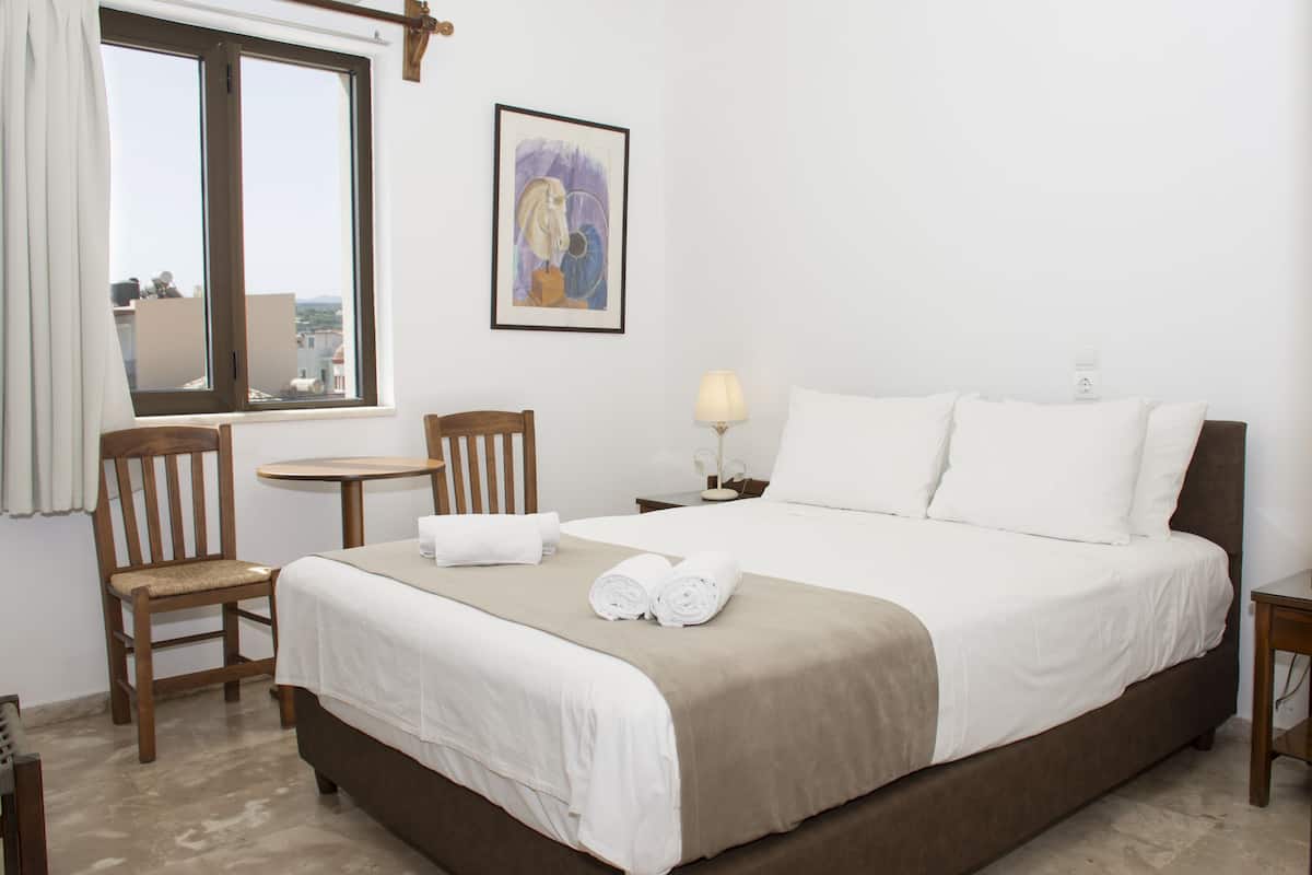 Habitación de hotel con cama, dos sillas, una mesita, lámpara y un cuadro en la pared.