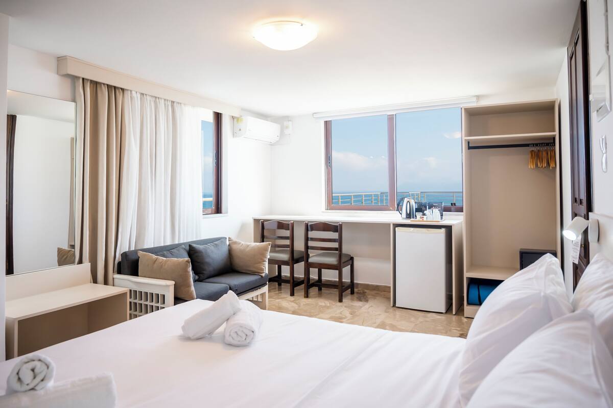 Habitación de hotel con cama, escritorio, silla, armario y vista al mar.