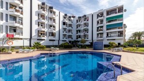 Un immeuble d’appartements moderne doté d’une piscine centrale, entourée de chaises longues.